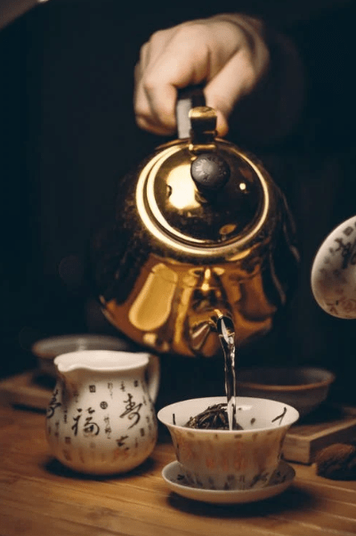 A person pouring water from the teapot into the cup