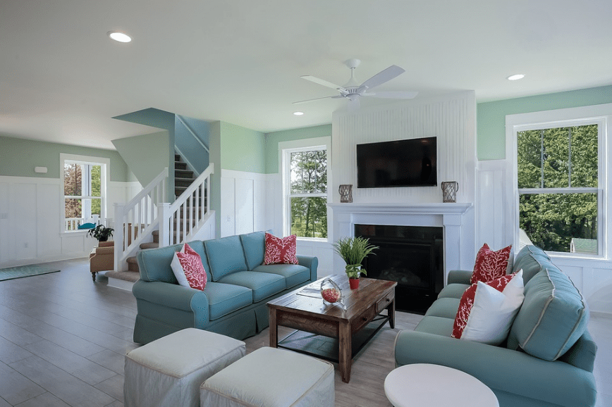 teal-colored walls, two couch facing each other, huge television in the middle, stairs with white railings