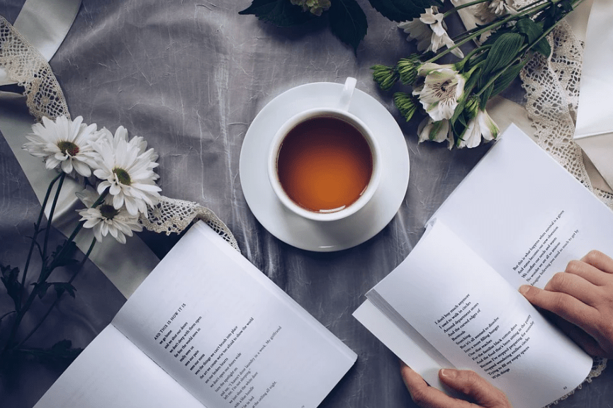 a cup of coffee, white flowers, a hand on a book