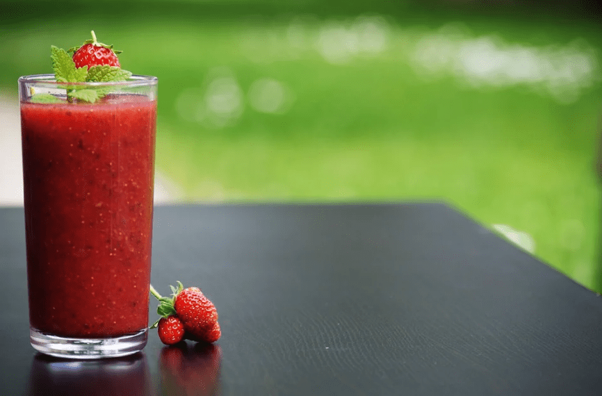 a glass of strawberry smoothie, strawberries, tabletop, grass