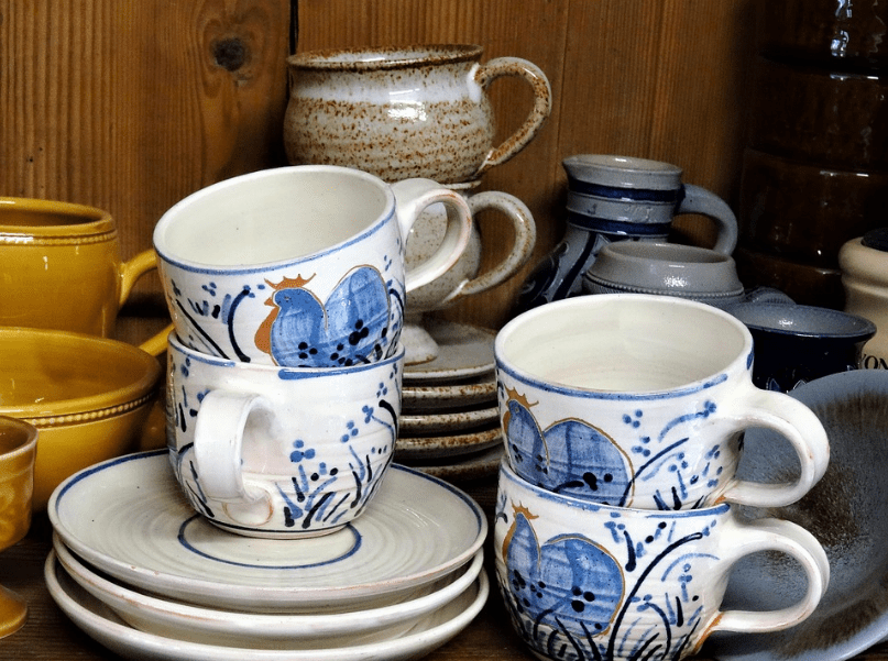 numerous mugs in different colors, pile of plates, wooden shelf