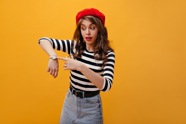 surprised-lady-red-beret-points-watch-cute-young-woman-with-bright-lips-pretty-hat-posing-orange-background