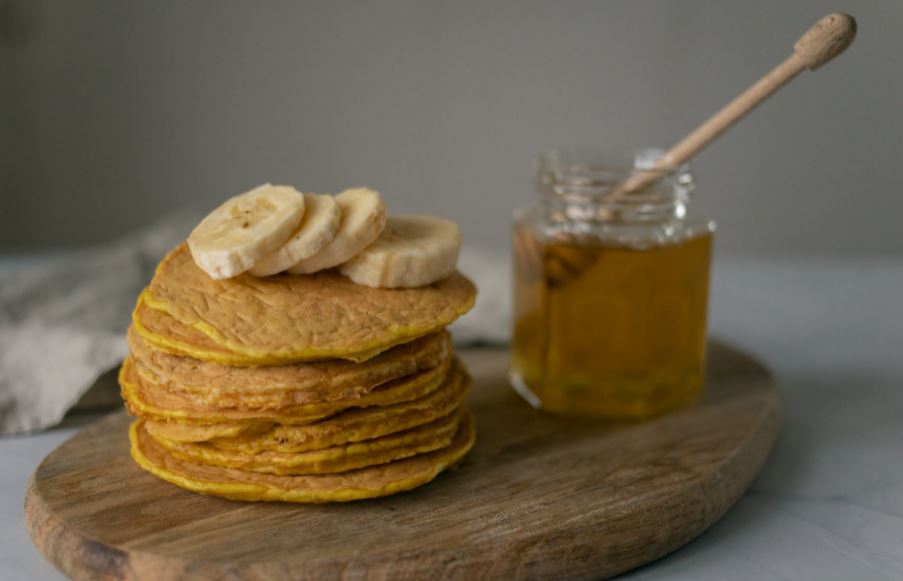 pancakes with bananas on chopping board near a jar of honey on table